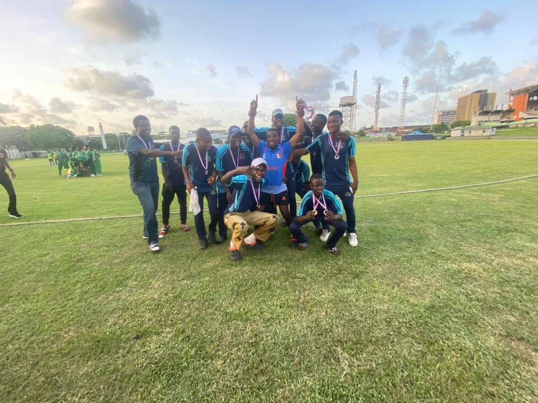 IMCC players celebrating on the field with medals and a trophy